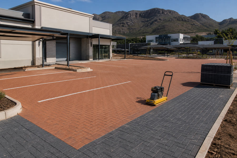 Terracotta herringbone commercial parking apron with charcoal borders at a Durbanville business park, plate compactor on the finished section.