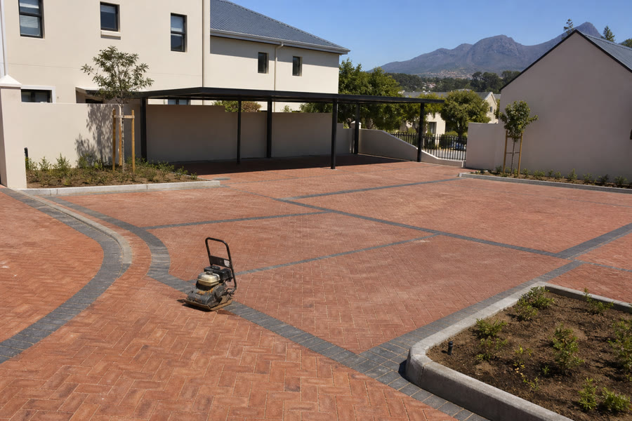 Terracotta herringbone visitor parking field with charcoal borders and plate compactor at a Durbanville suburban complex.
